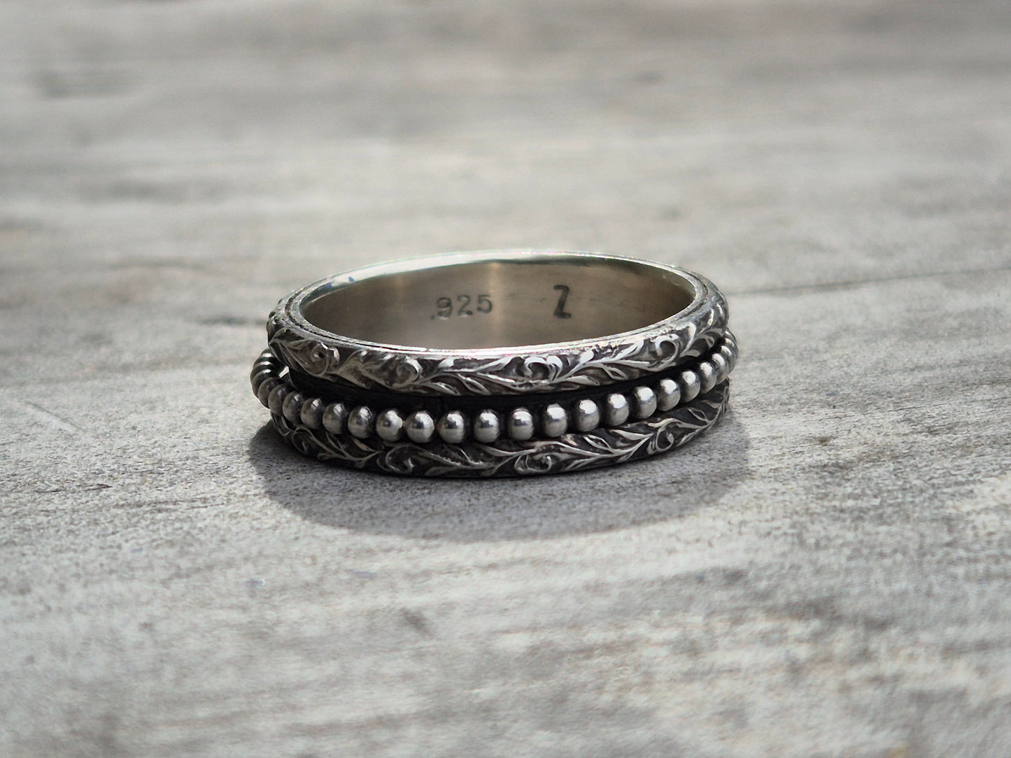 A handmade sterling silver spinner ring with two detailed bands and beaded inner band. The ring has been blackened