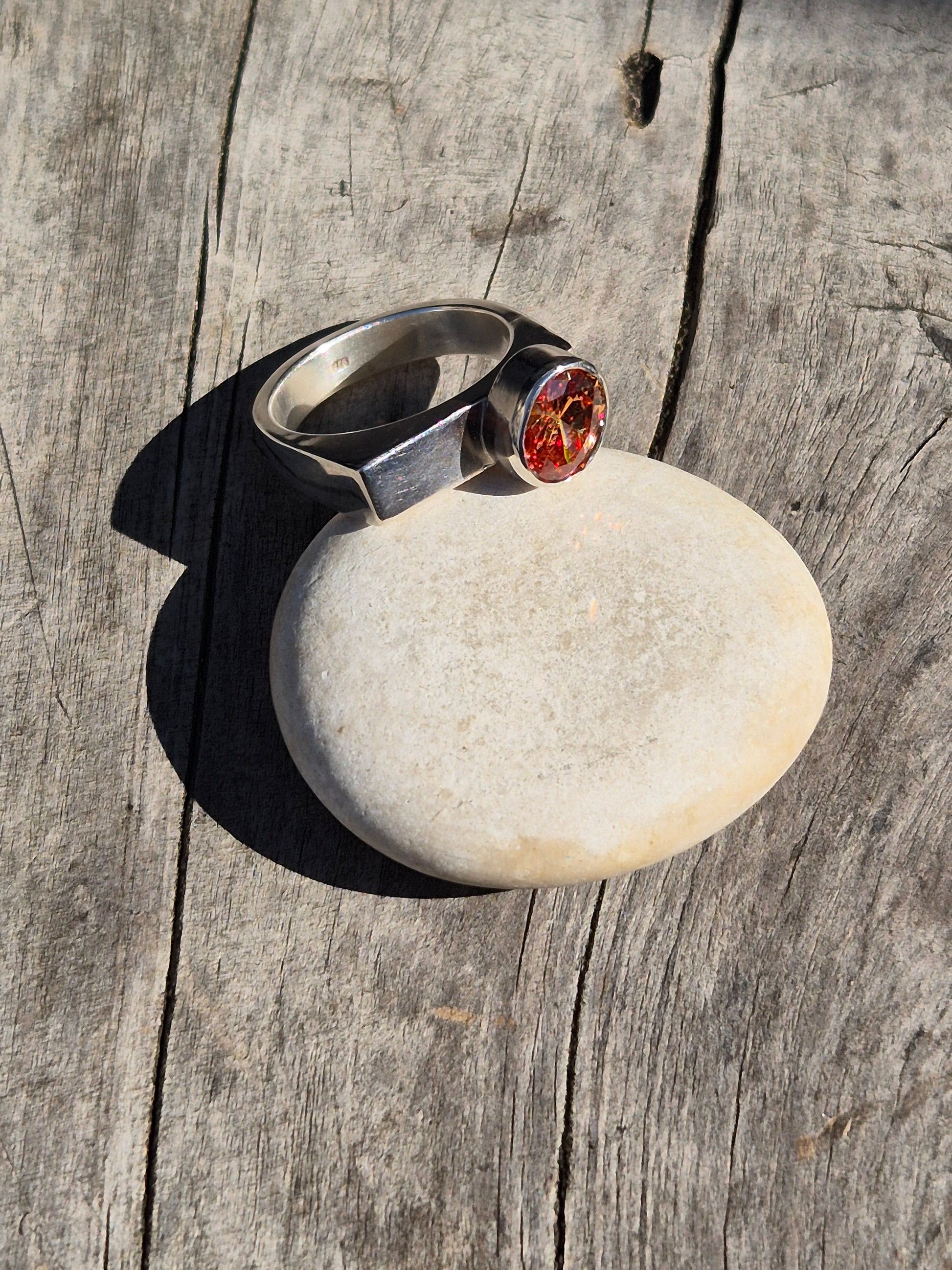 A Sterling Silver and Champagne Cubic Zirconia Ring with a sleek modern design, featuring a round, warmed champagne-colored gemstone set on a narrow silver band, placed on a textured wooden surface.