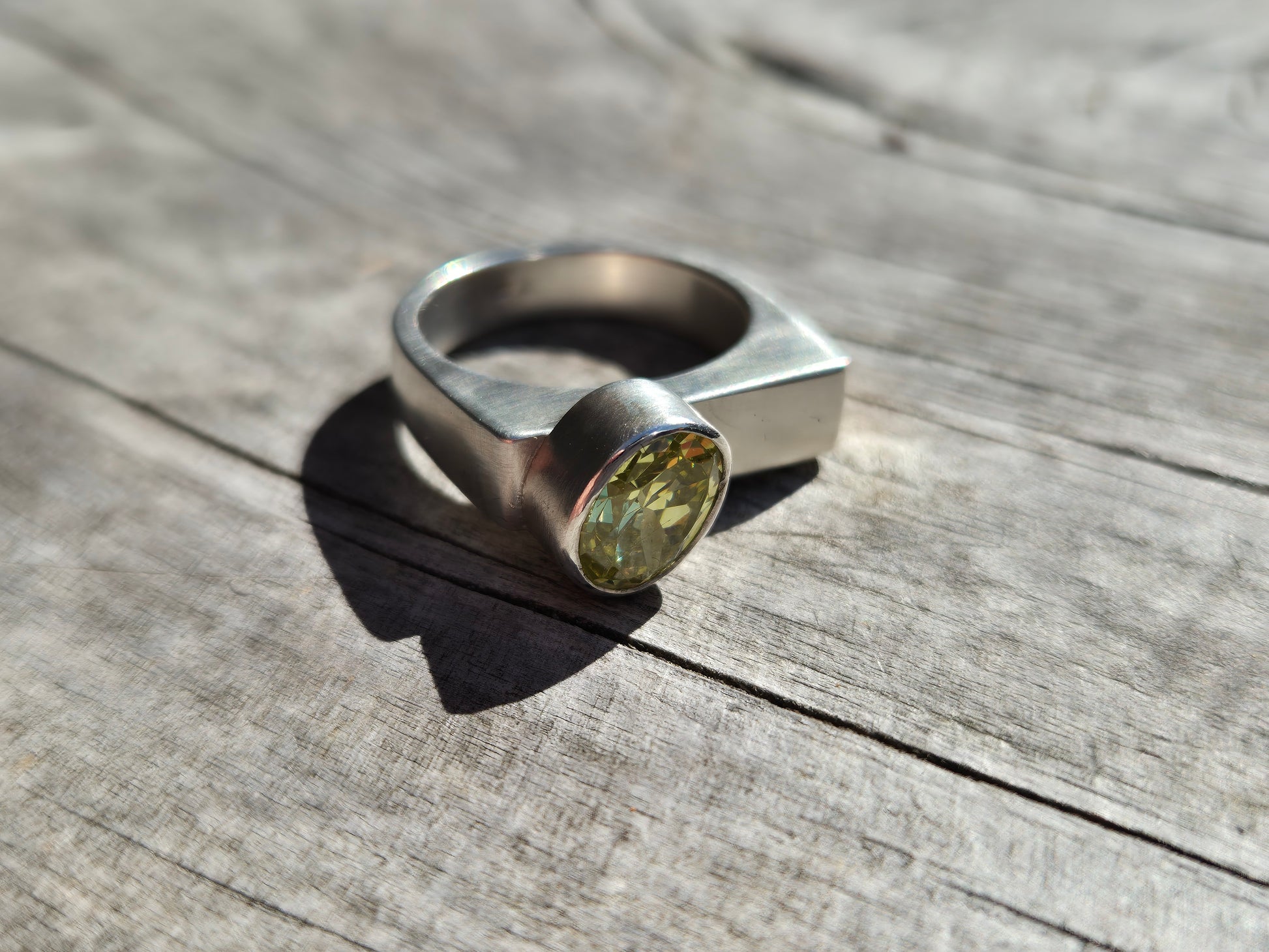 A Sterling Silver ring with a brushed satin finish and an acid green cubic zirconia set on a wooden surface.