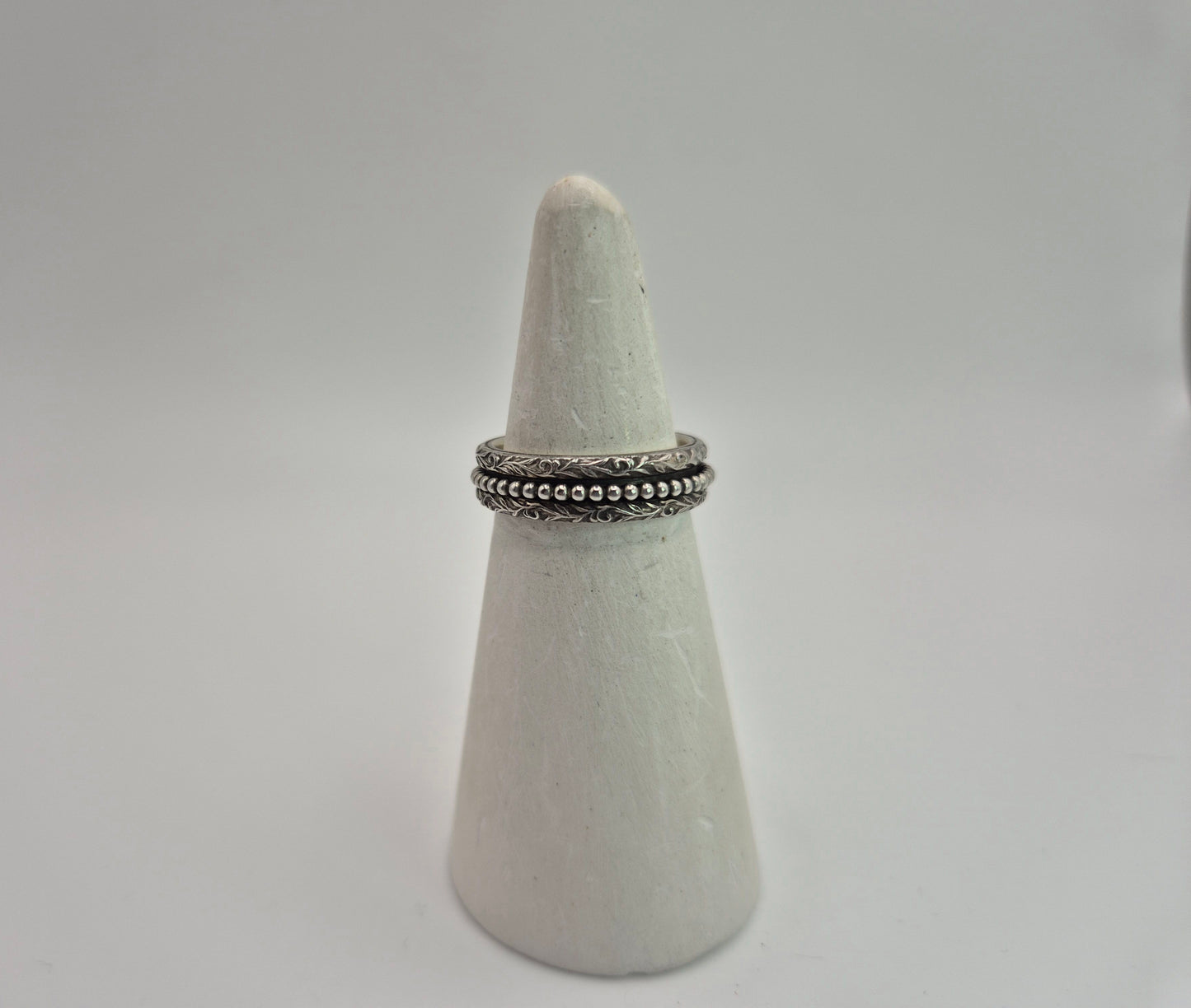 Detailed sterling silver spinner ring with beaded inner band on white ring cone